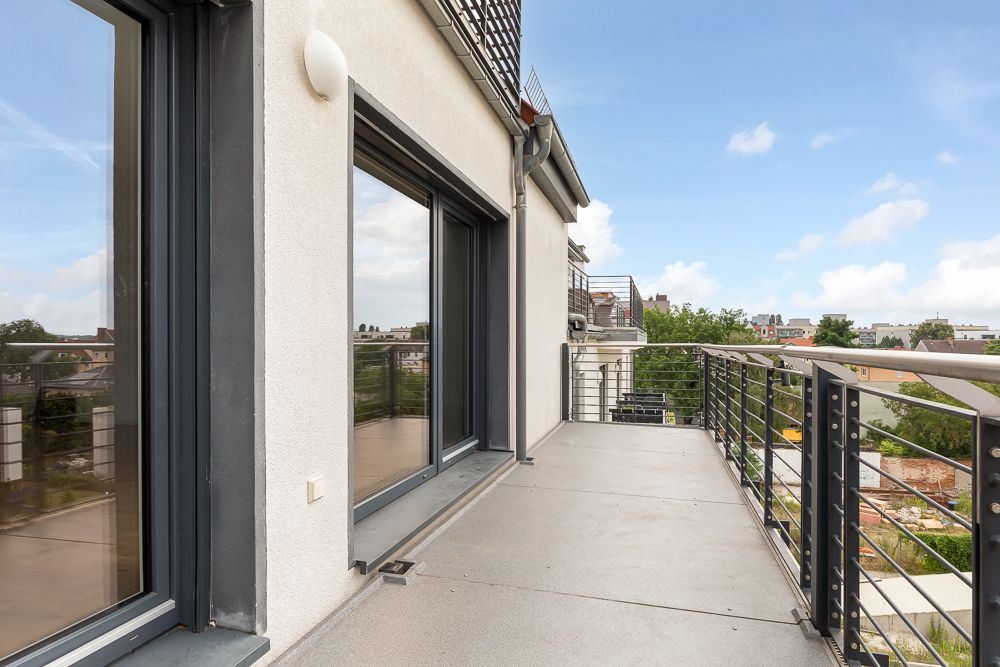 Großer Balkon mit Metallgeländer und Blick auf benachbarte Häuser und Bäume.