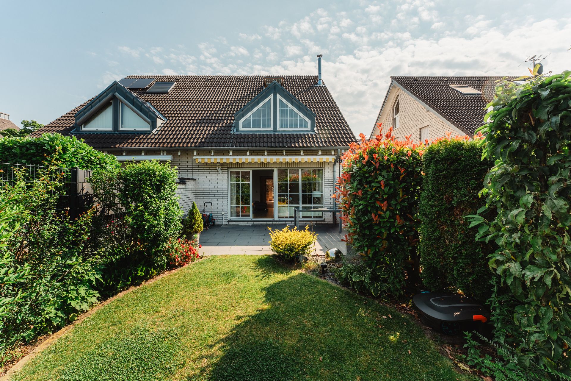 Blick auf ein Einfamilienhaus mit Terrasse und gepflegtem Garten mit Hecken.