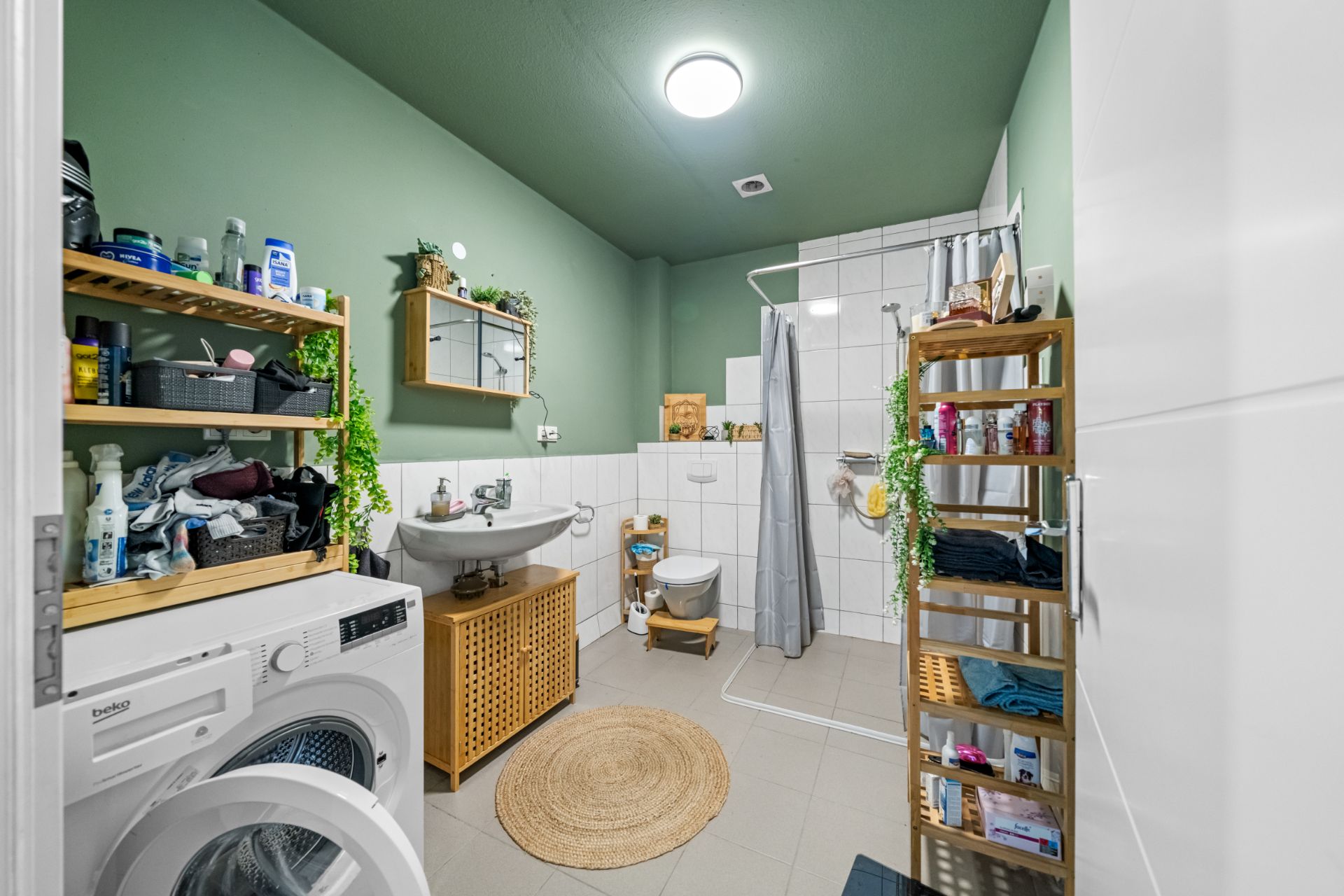 Modernes Badezimmer mit Dusche, Waschmaschine, Regal und grün gestrichenen Wänden.