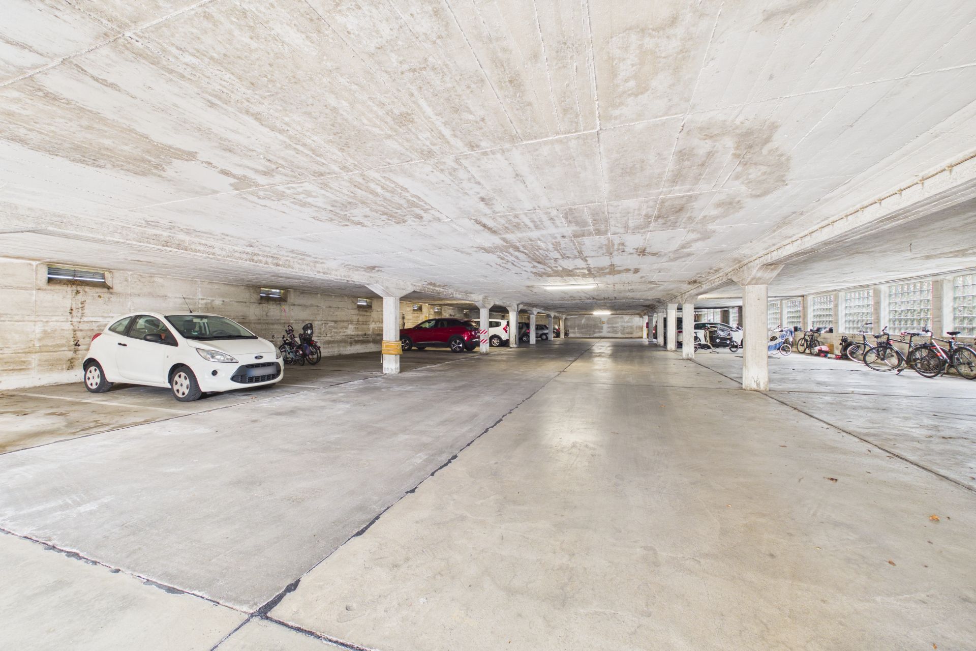 Helle Tiefgarage mit geparkten Autos und Fahrrädern entlang der Seitenwände.