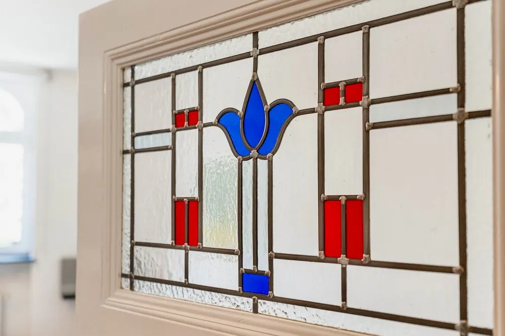 Nahaufnahme eines Fensters mit buntem Glas und geometrischem Muster in Blau und Rot.