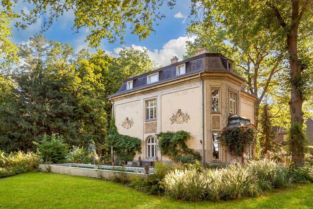 Großes, zweistöckiges Wohnhaus mit Mansardendach, umgeben von Garten und Bäumen.