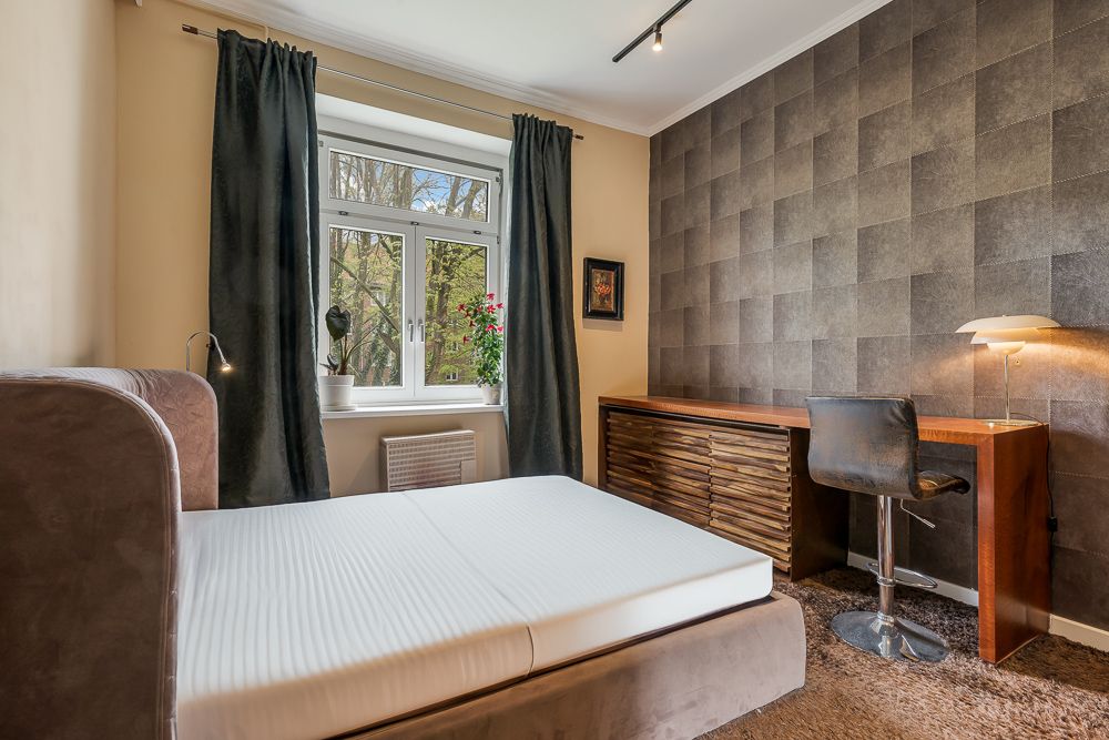 Schlafzimmer mit Doppelbett, Schreibtisch, Stuhl und Fenster mit Vorhängen.