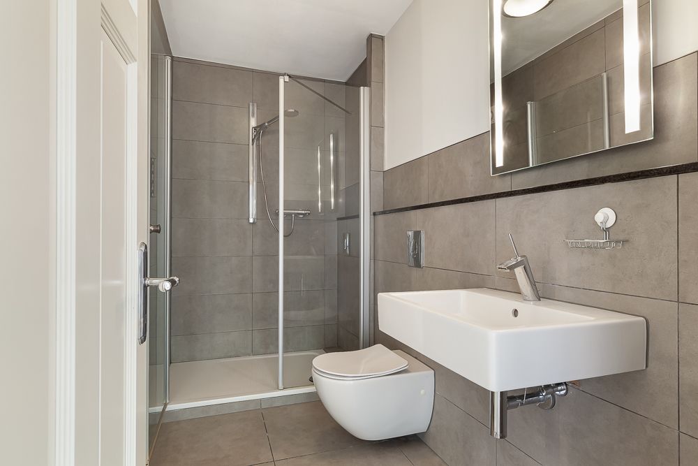 Modernes Bad mit Dusche, Wandtoilette, Waschbecken und Spiegel.