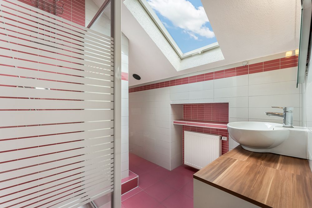 Modernes Bad mit Dachfenster, Waschtisch, Glasdusche und rosa-weißen Fliesen.
