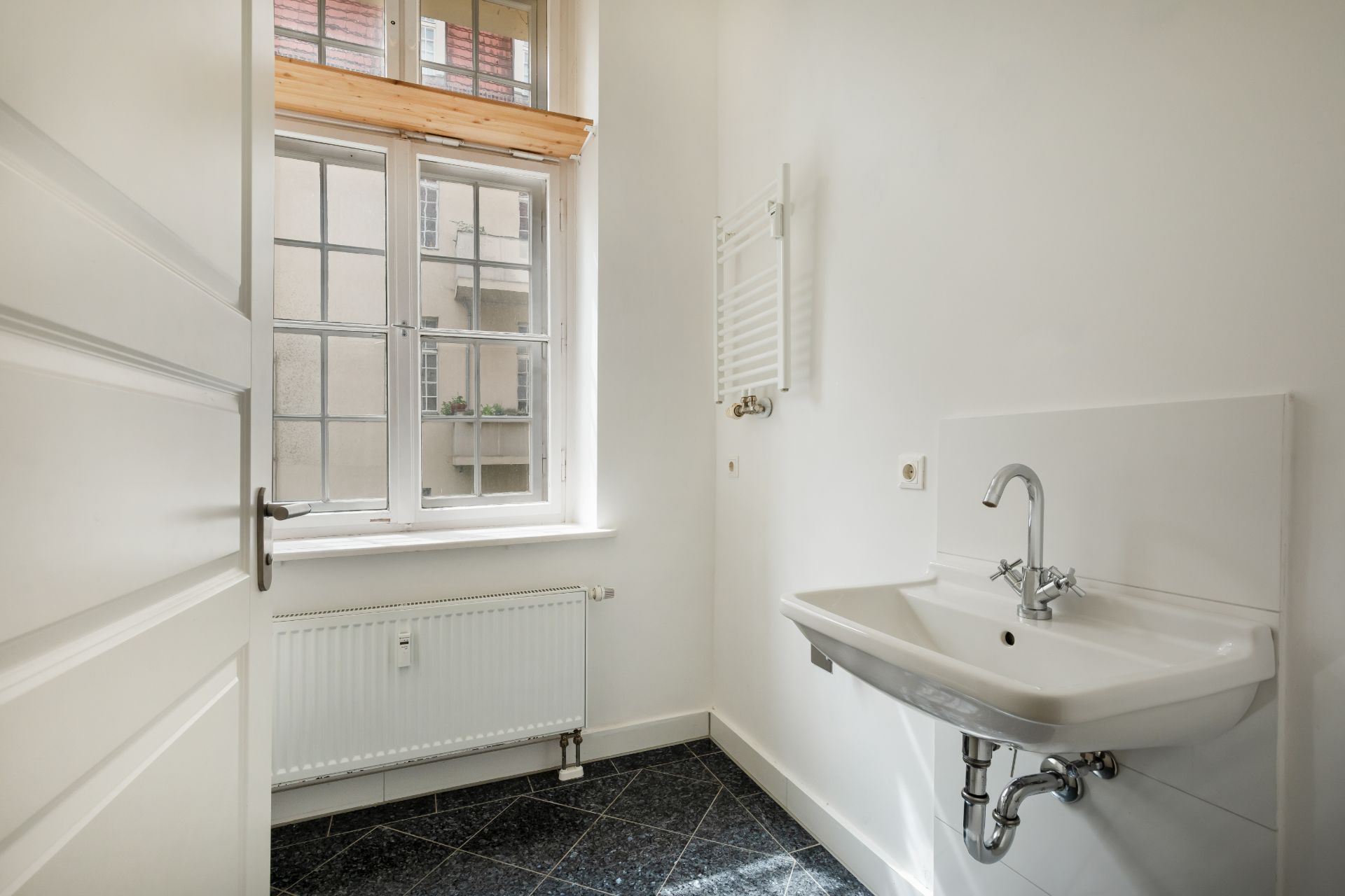 Heller Raum mit Fenster, Waschbecken, Heizkörper und weißer Wand.