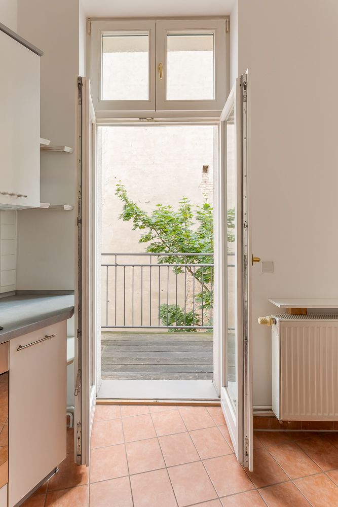 Geöffnete Tür in einer Küche führt auf einen kleinen Balkon mit Geländer und Blick auf einen Baum.