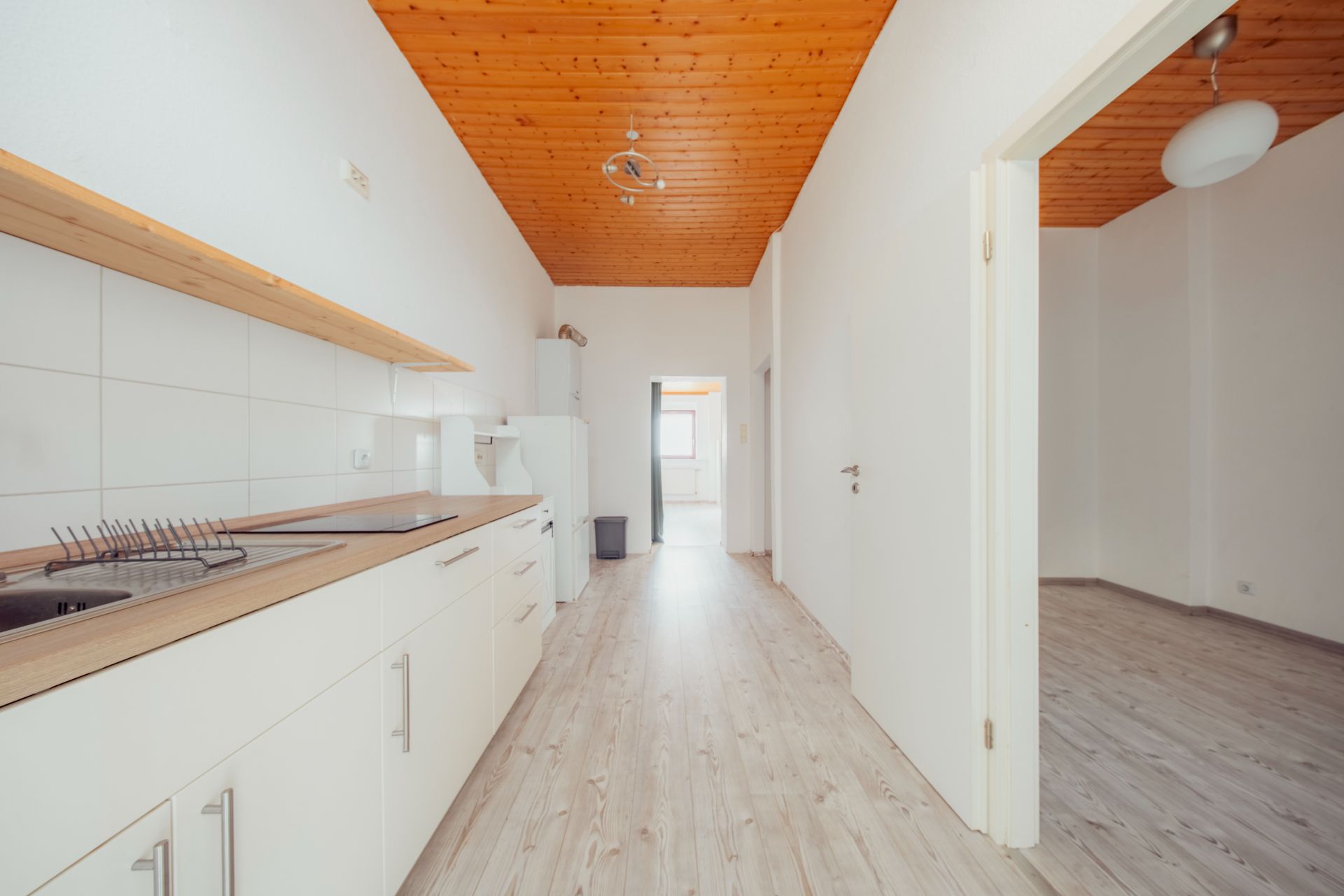 Helle Küche mit weißen Schränken, Holzdecke und Zugang zu einem angrenzenden Raum.