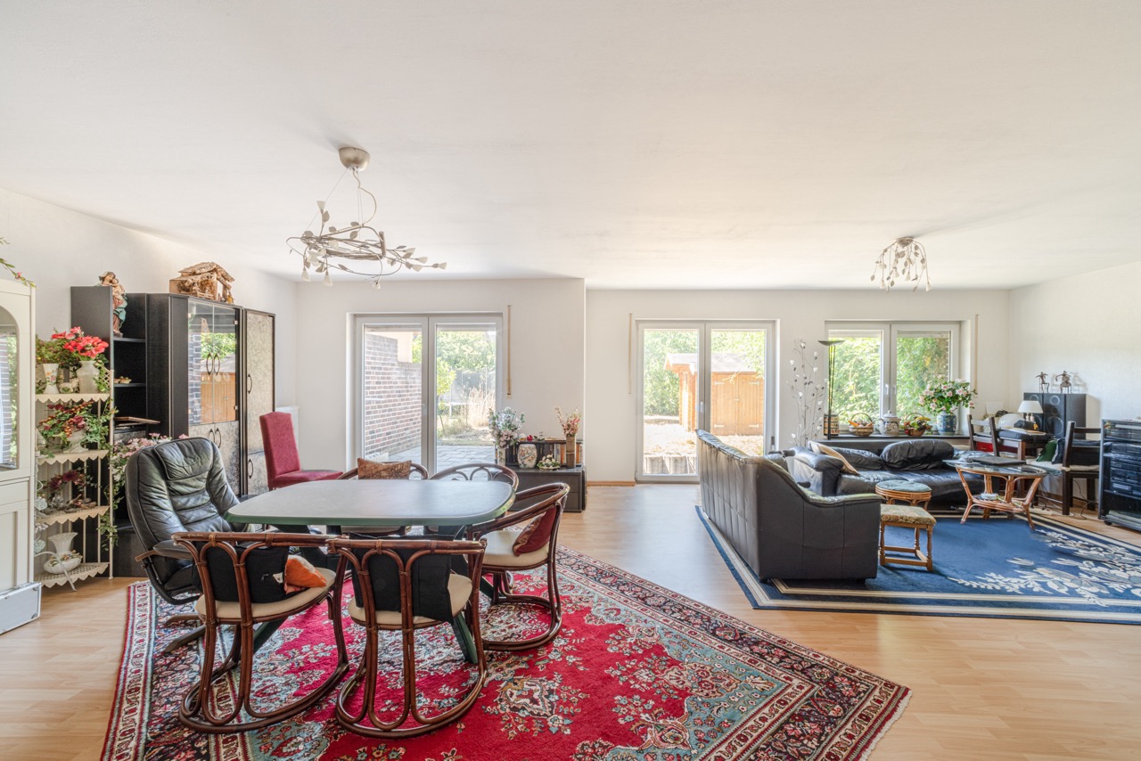 Großes Wohnzimmer mit Essbereich, zwei Teppichen, Ledersofa, Esstisch und großen Fenstern zum Garten.