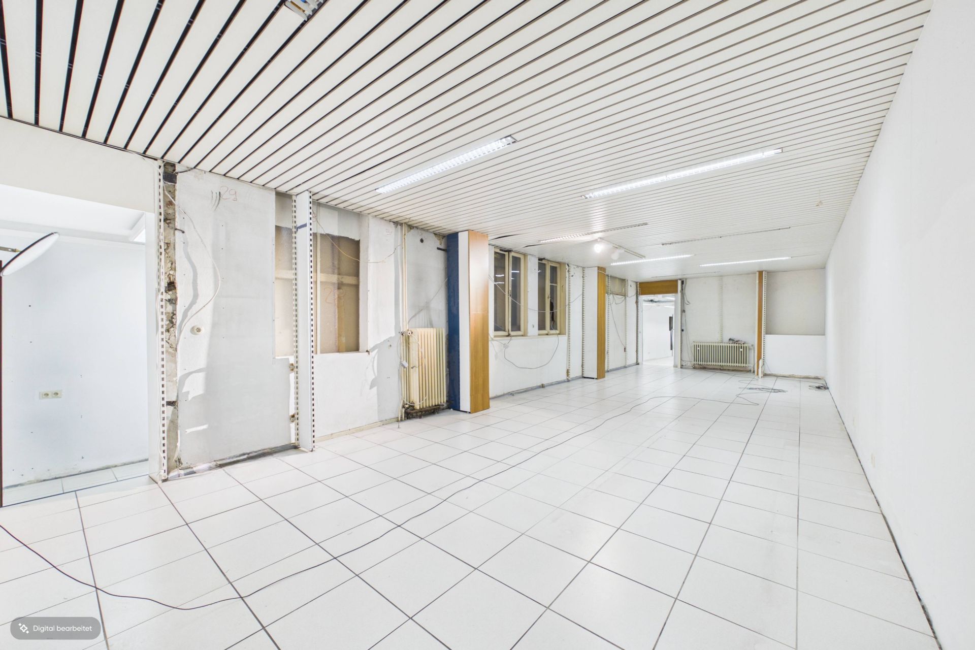 Leerer, großer Raum mit weißen Fliesen, weißen Wänden und abgehängter Decke.