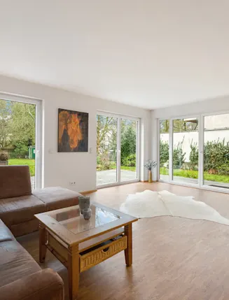 Helles Wohnzimmer mit großer Eckcouch, Glastisch und bodentiefen Fenstern zum Garten.