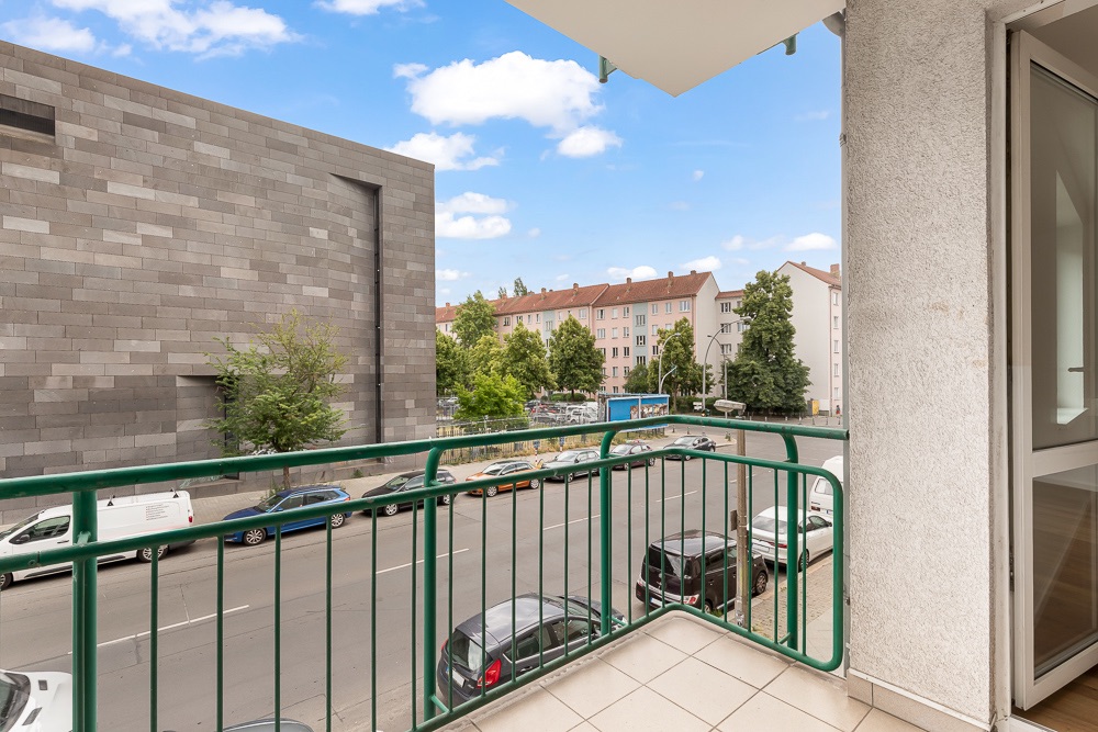 Balkon mit grünem Geländer, Blick auf Straße, geparkte Autos und Wohnhäuser.