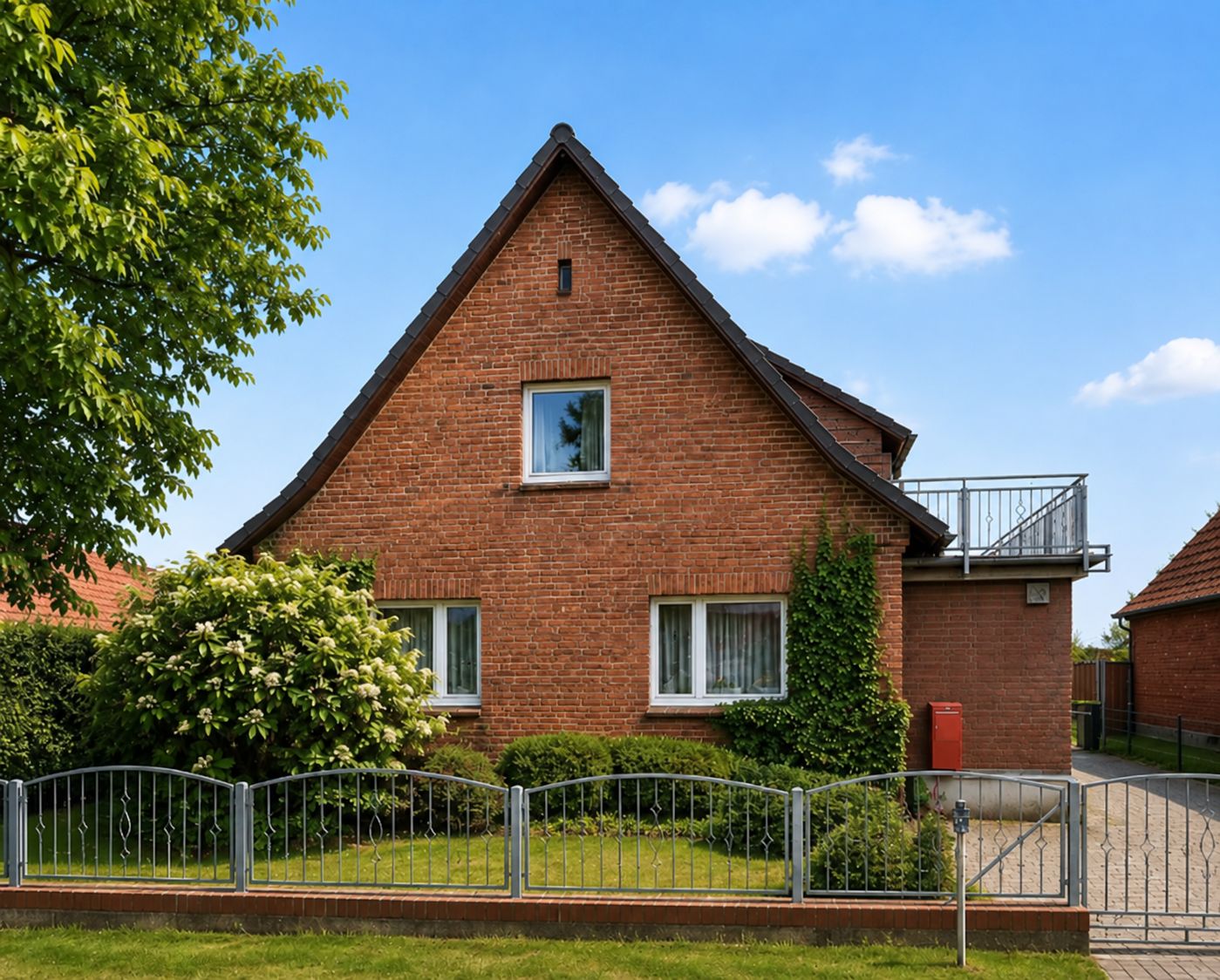 Backstein-Einfamilienhaus mit Satteldach, kleinem Garten und Zaun im Vordergrund.