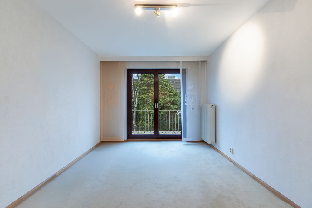 Leeres Zimmer mit Teppichboden, Glas-Doppeltür und Zugang zu einem kleinen Balkon.