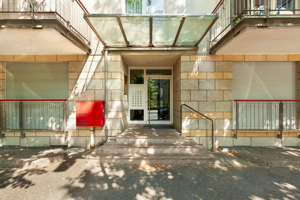 Hauseingang mit Glasvordach, Treppe, Geländer und geschlossenen Rollläden.