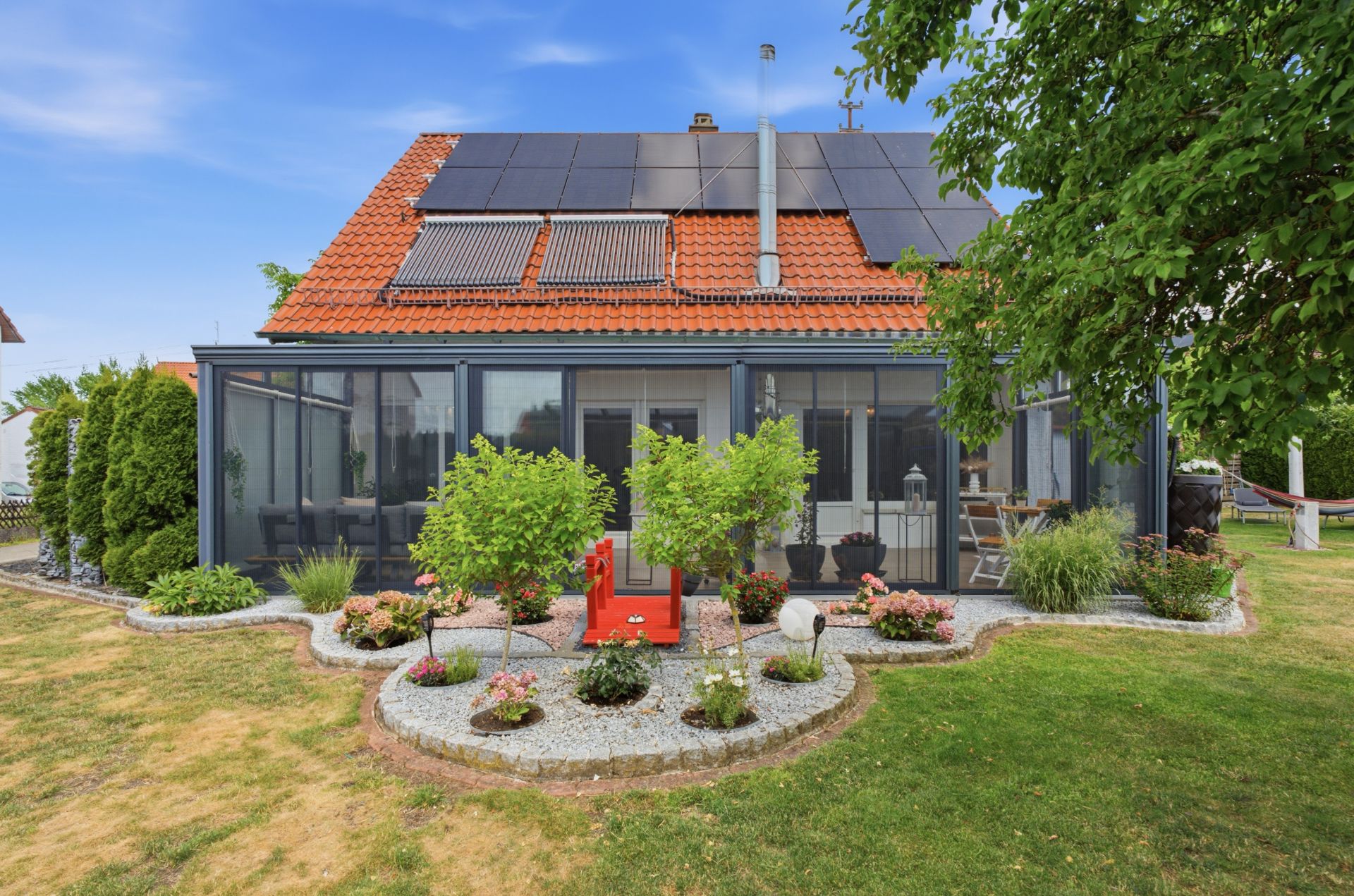 Einfamilienhaus mit Wintergarten, Garten und Solarpaneelen auf dem Dach.