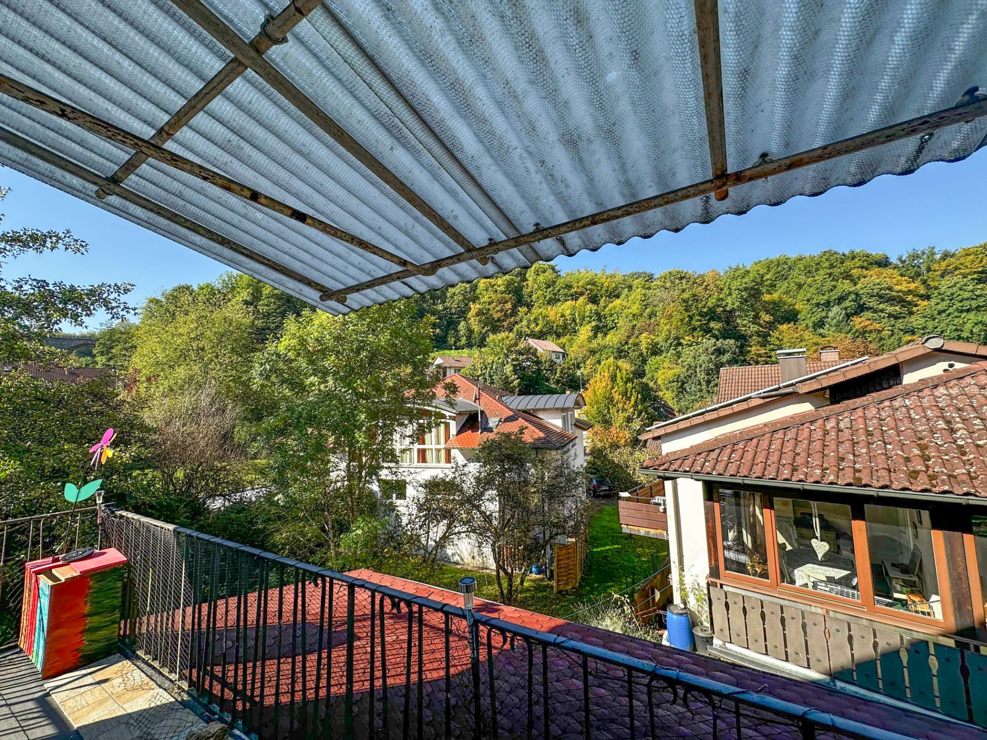 Balkon mit Überdachung, Blick auf Nachbarhäuser, Bäume und bewaldeten Hügel.