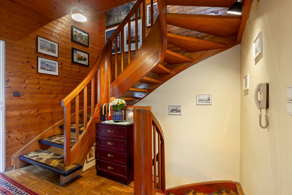 Holztreppe im Flur mit Gemälden an der Wand und einer Kommode mit Blumen.