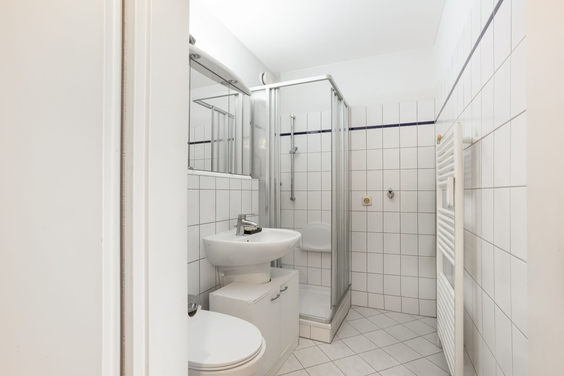 Modernes Badezimmer mit Dusche, Waschbecken, WC, Spiegel und weißen Fliesen.