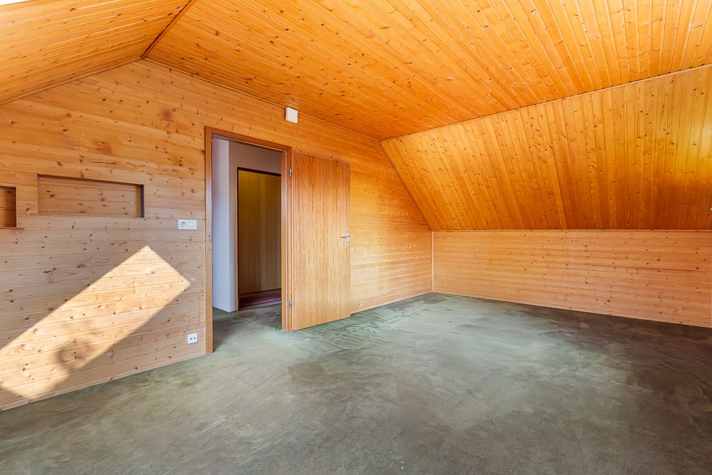 Zimmer mit Holzverkleidung an Wänden und Decke, offenem Türrahmen und grauem Boden.