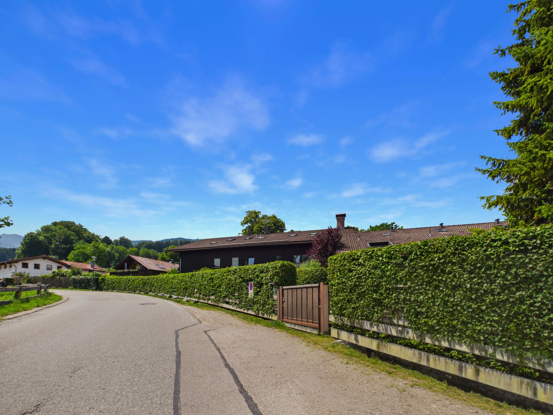 Gepflegte Straße mit Hauseingangstor und hoher grüner Hecke vor Wohngebäuden.