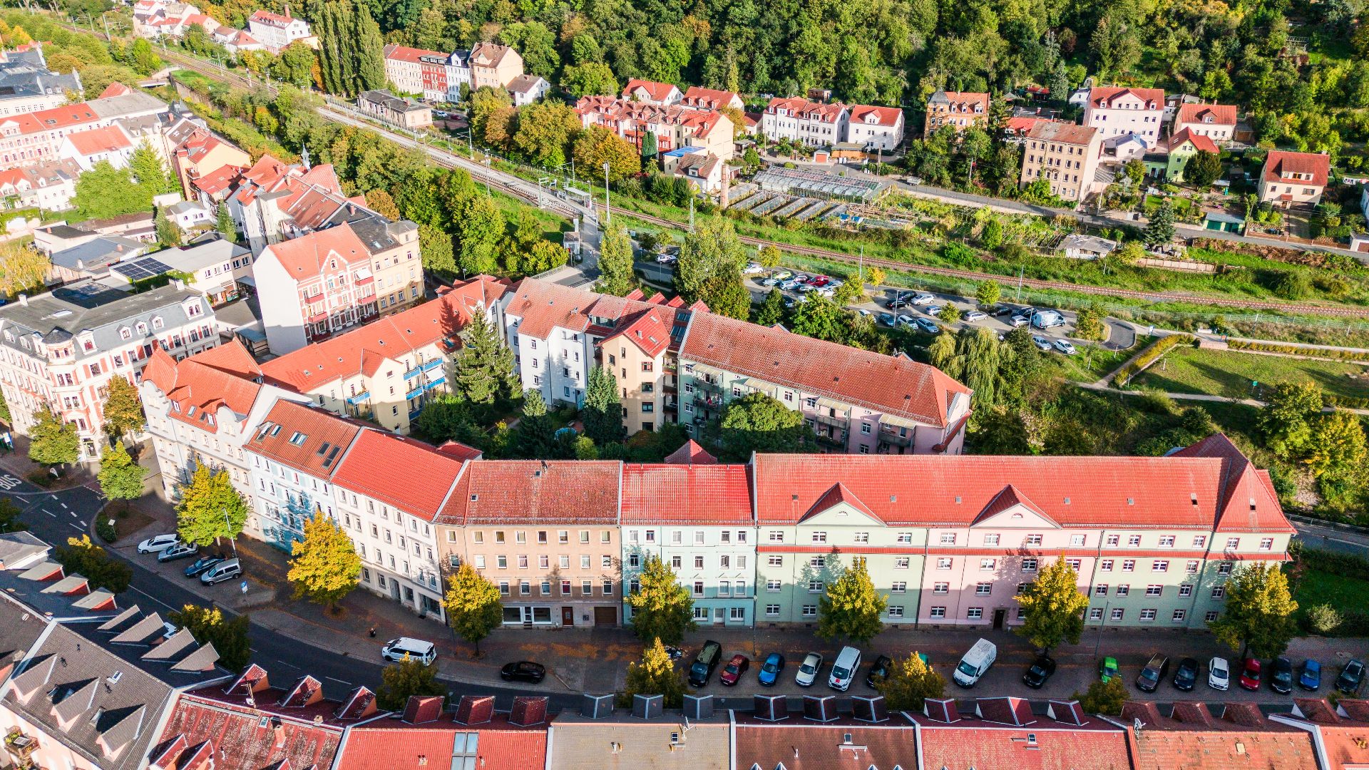 Luftaufnahme von Wohnhäusern mit roten Dächern, Bäumen und geparkten Autos entlang einer Straße.