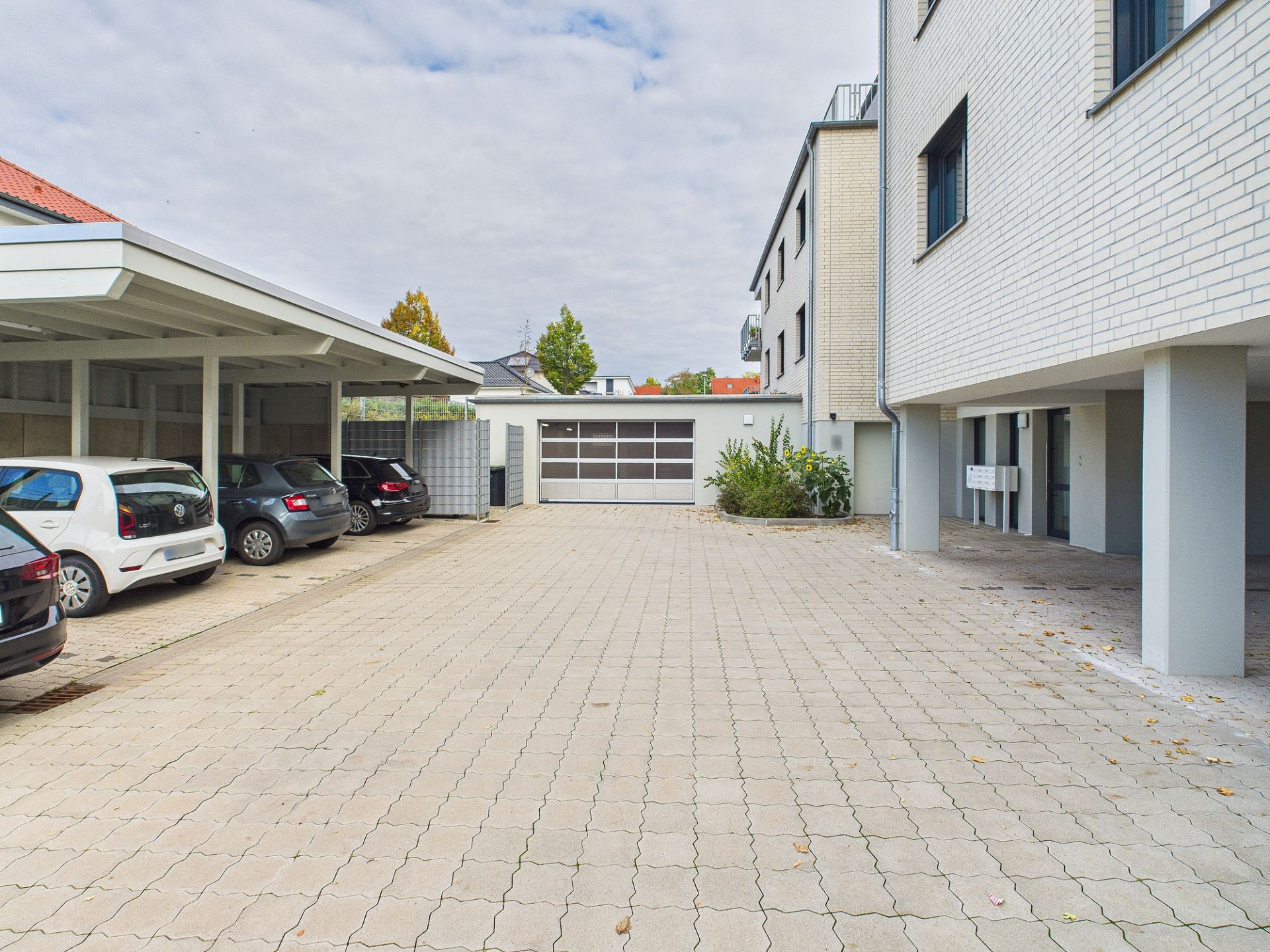 Gepflasterter Innenhof mit Carport und geparkten Autos neben einem Wohngebäude.