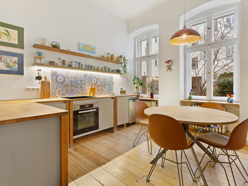 Moderne Küche mit Holzboden, Esstisch, bunten Fliesen und großen Fenstern.