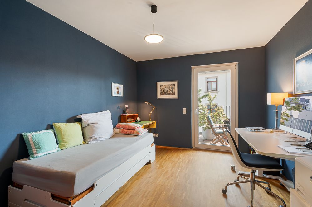 Modernes Zimmer mit Einzelbett, Schreibtisch, Stuhl und Zugang zu einem Balkon mit Pflanzen.
