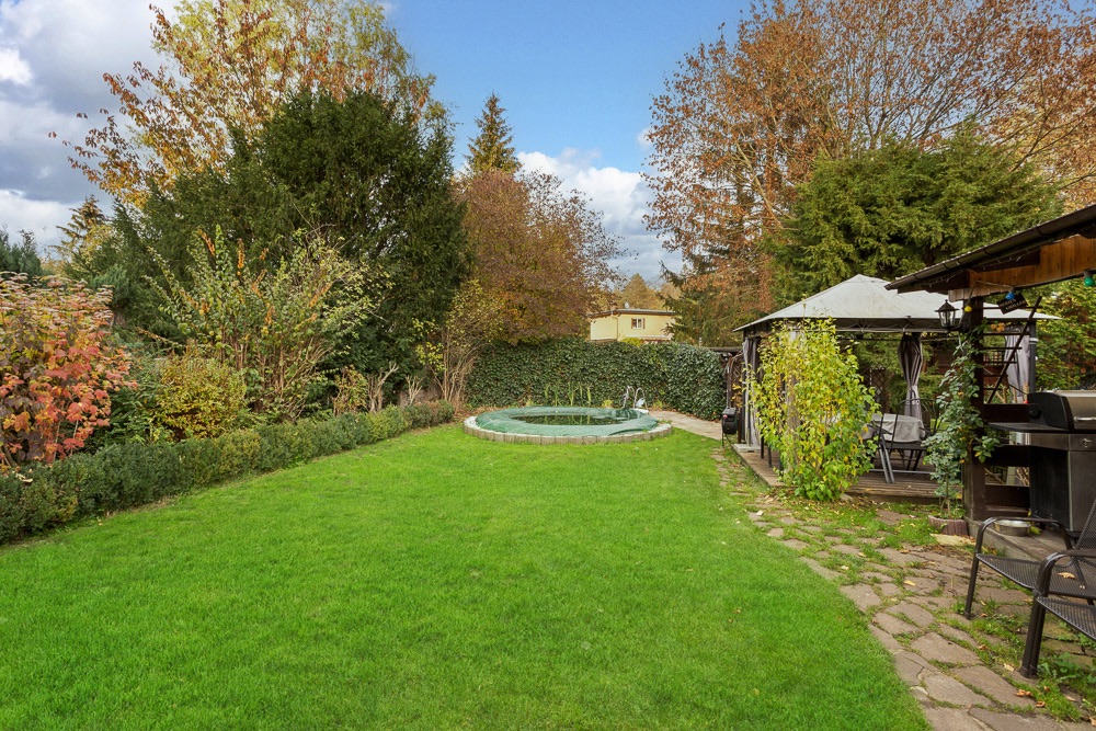 Garten mit grünem Rasen, rundem Pool und überdachtem Sitzbereich mit Grill.