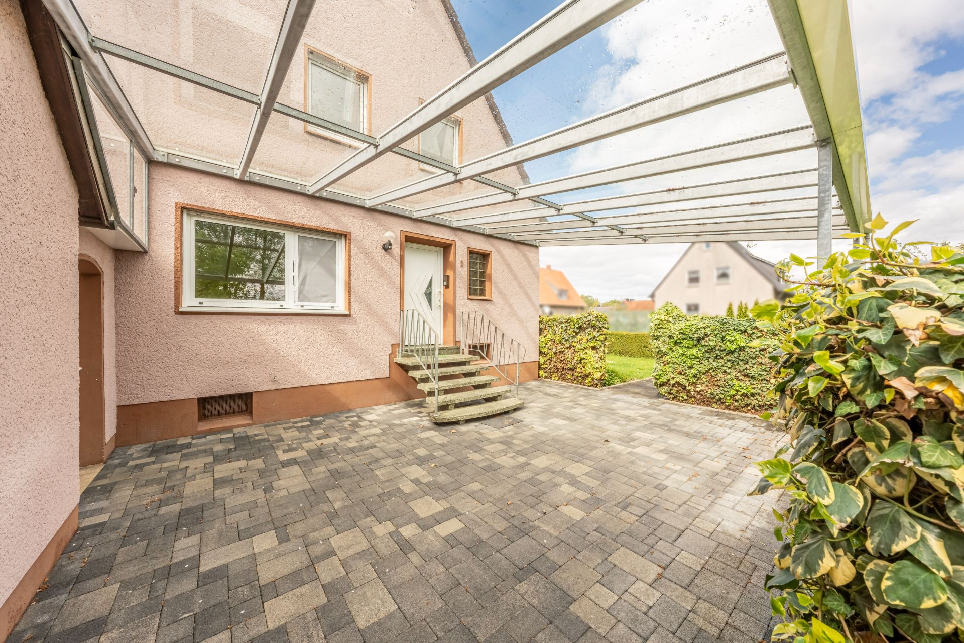 Überdachte Terrasse mit Pflastersteinen und Treppe zum Hauseingang.