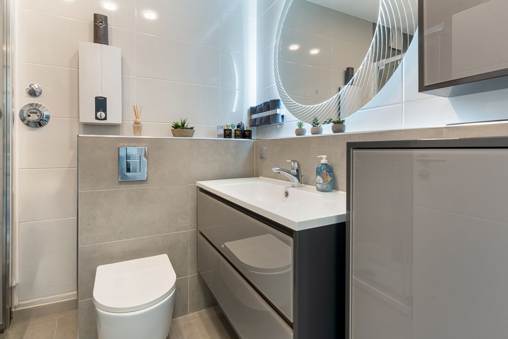 Modernes Badezimmer mit Waschbecken, Spiegel, Toilette und kleinen Pflanzen auf dem Regal.