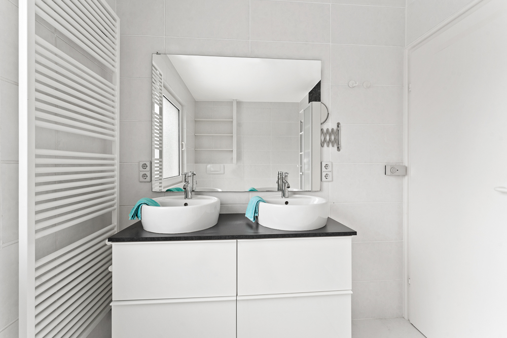 Modernes Badezimmer mit zwei Waschbecken, großem Spiegel und weißen Fliesen.
