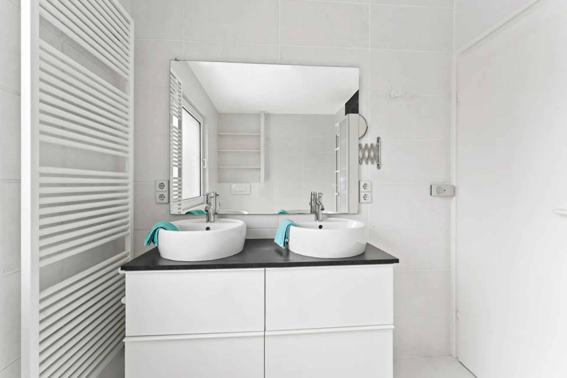 Modernes Badezimmer mit zwei Waschbecken, großem Spiegel und weißen Fliesen.
