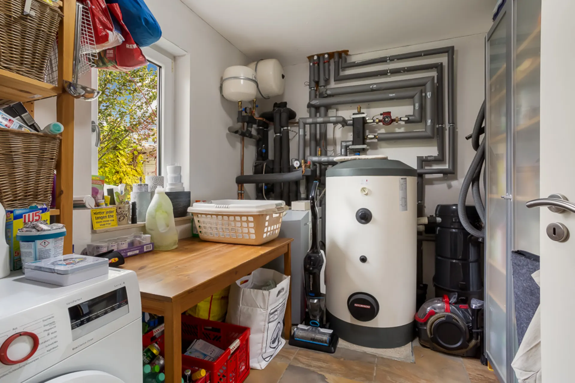 Hauswirtschaftsraum mit Waschmaschine, Heizungsanlage, Regalen und Haushaltsgegenständen.