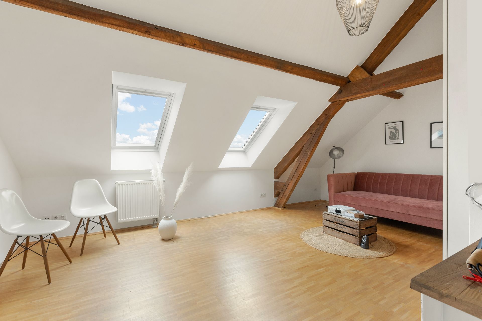 Heller Dachraum mit Sofa, zwei Stühlen, Holzdecke und zwei Dachfenstern.