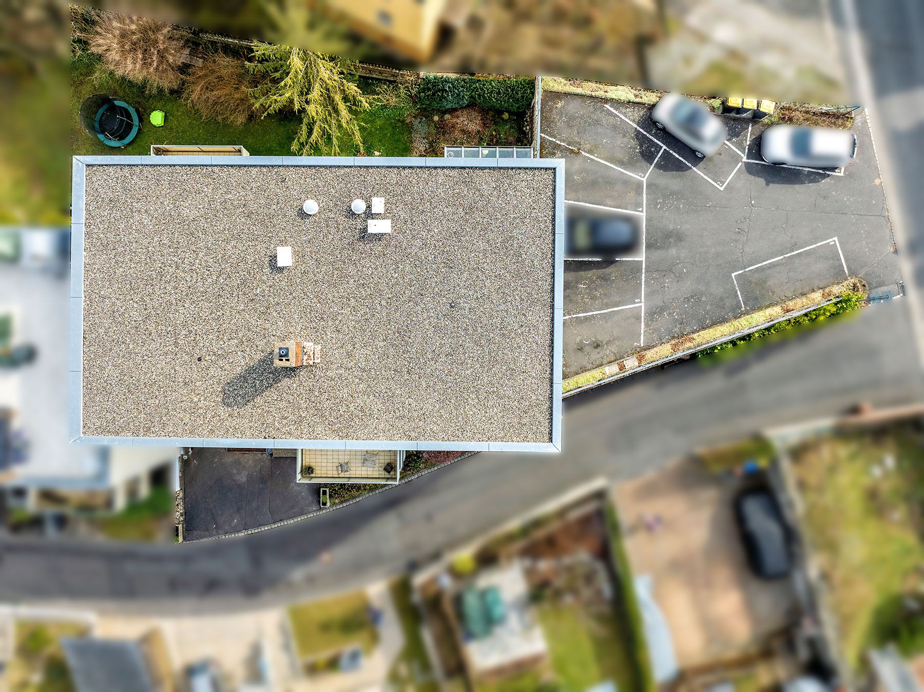 Luftaufnahme eines Flachdachhauses mit angrenzendem Parkplatz und einigen geparkten Autos.