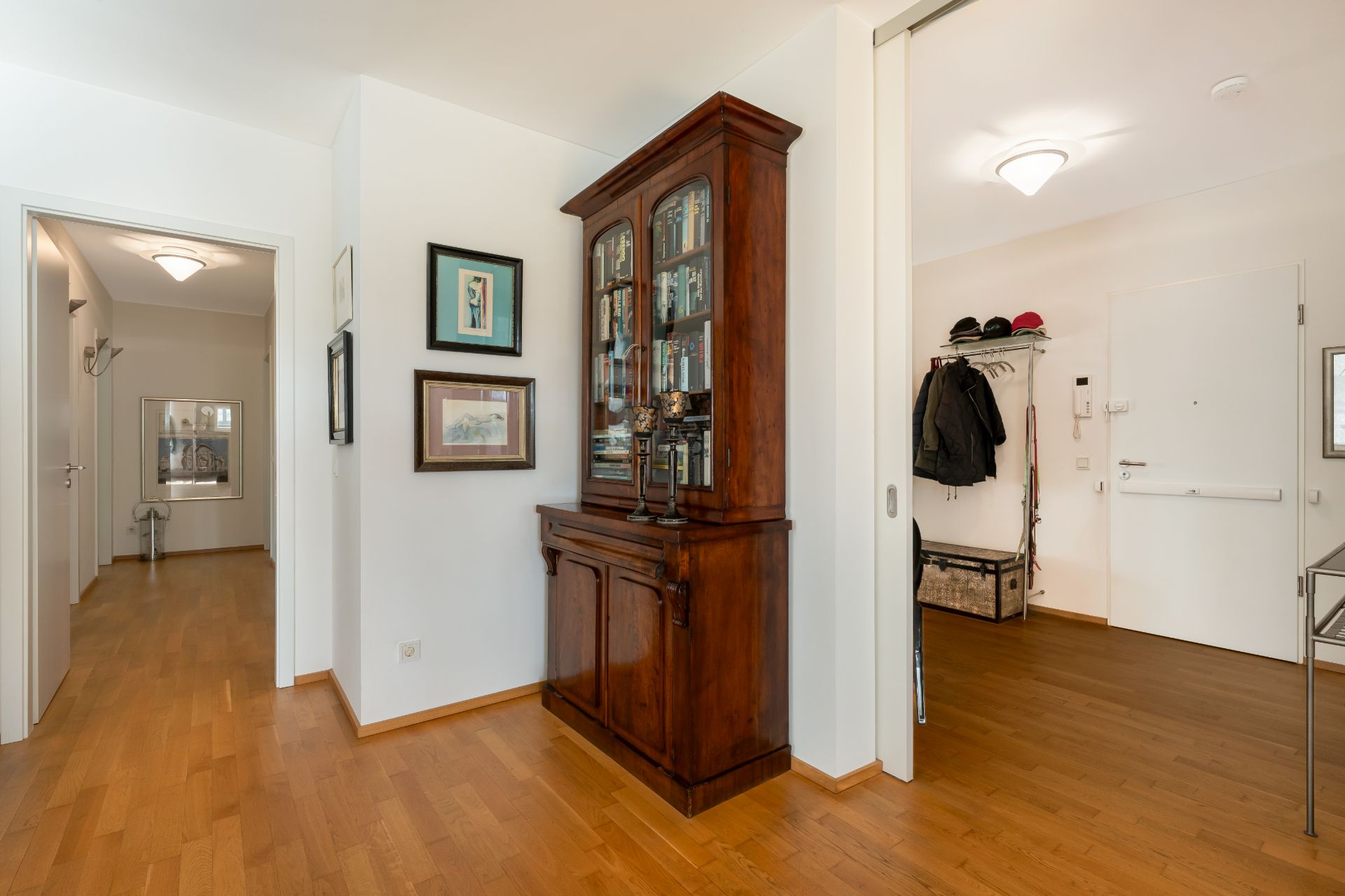 Flur einer Wohnung mit Holzboden, Vitrine, Garderobe und Bildern an der Wand.