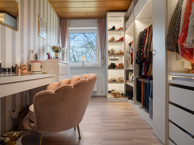 Ankleidezimmer mit Schminktisch, rosa Sessel, Kleiderschrank und Fenster mit Blick ins Freie.