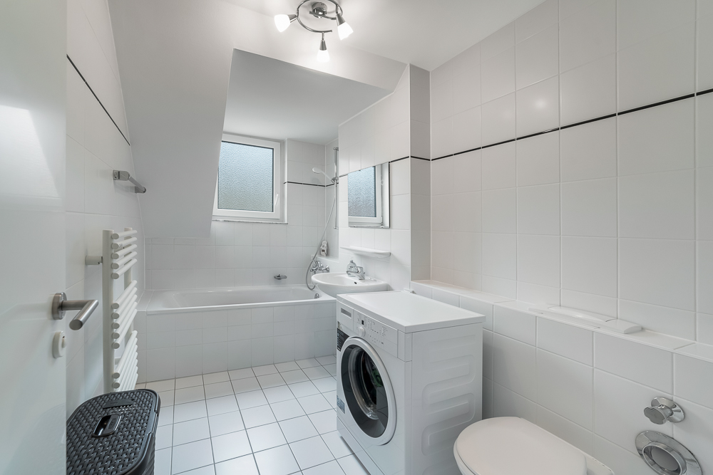Modernes Badezimmer mit Badewanne, Waschmaschine, Toilette und Waschbecken, alles in Weiß gehalten.