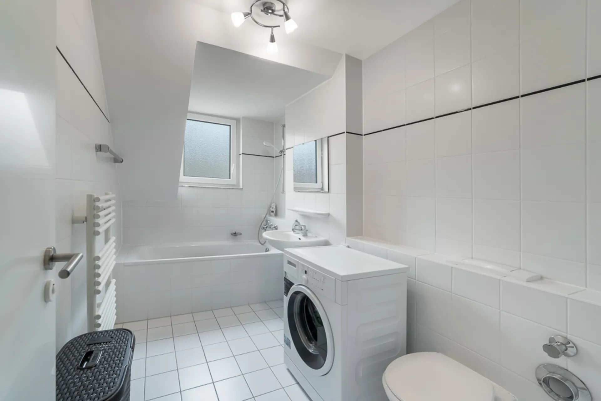 Modernes Badezimmer mit Badewanne, Waschmaschine, Toilette und Waschbecken, alles in Weiß gehalten.