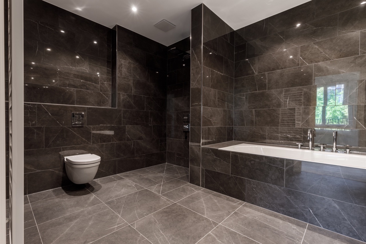 Modernes Badezimmer mit dunklen Fliesen, Wandtoilette und Badewanne.
