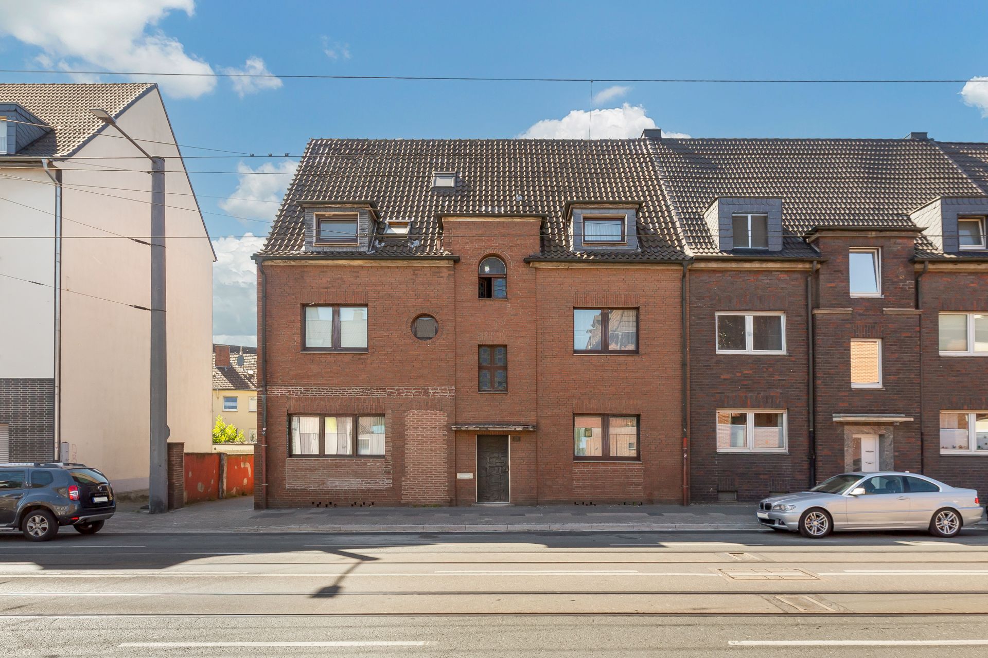Dreistöckiges Wohnhaus mit roter Backsteinfassade und mehreren Fenstern an einer Straße.