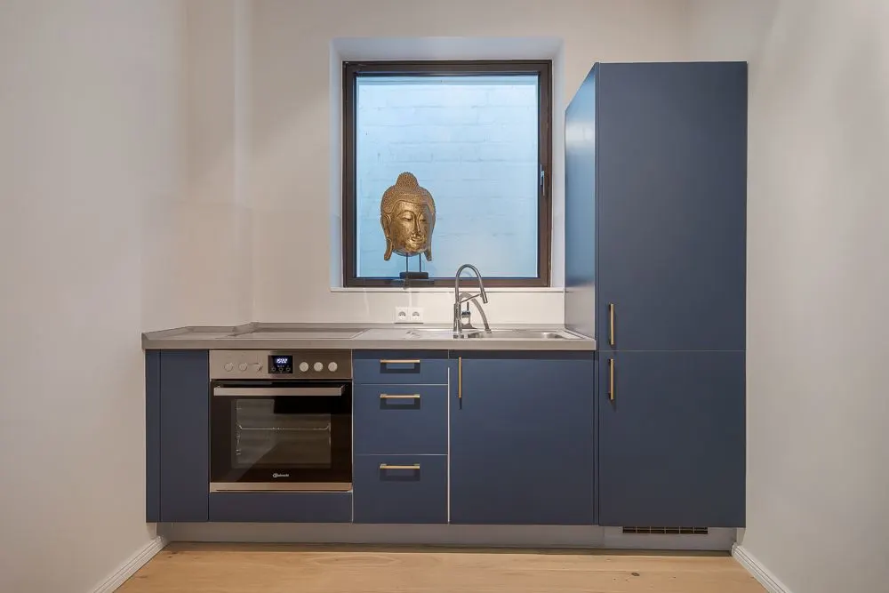 Moderne blaue Einbauküche mit Backofen, Spüle und Fenster mit goldener Skulptur.