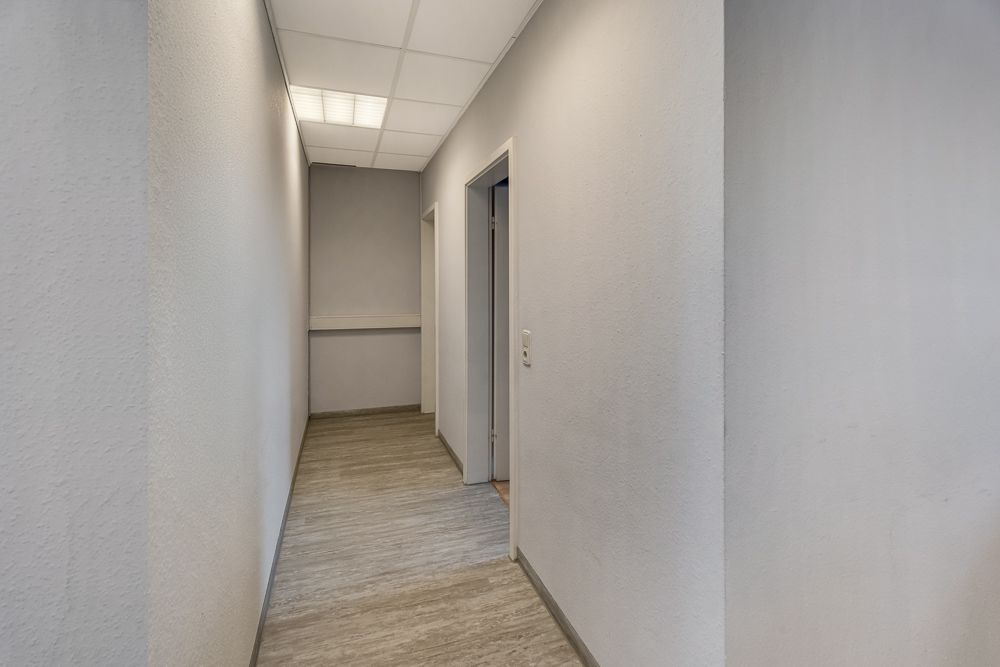 Heller Flur mit grauen Wänden, Deckenleuchten und mehreren offenen Türen.