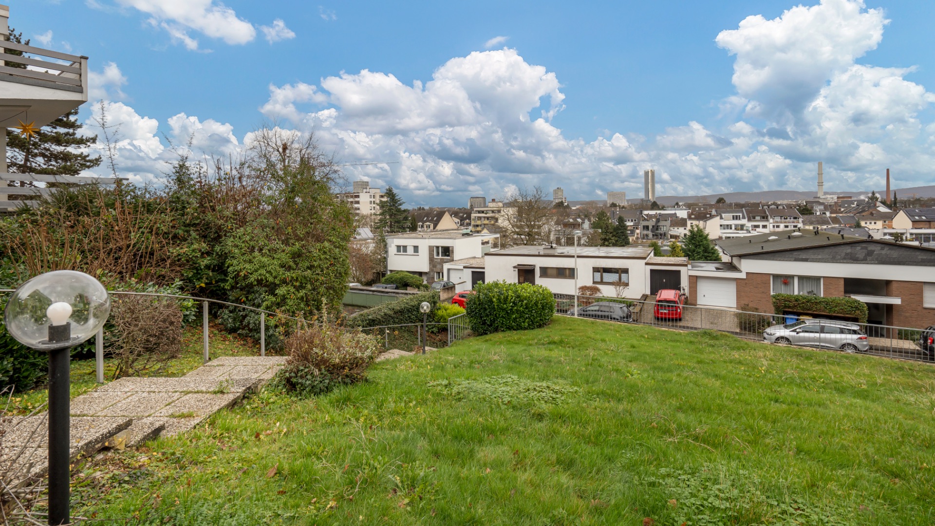 Grüner Garten mit Weg und Blick auf Wohnhäuser und Stadt im Hintergrund.