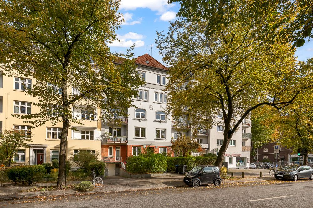 Mehrstöckiges Wohnhaus mit Balkonen an einer von Bäumen gesäumten Straße.