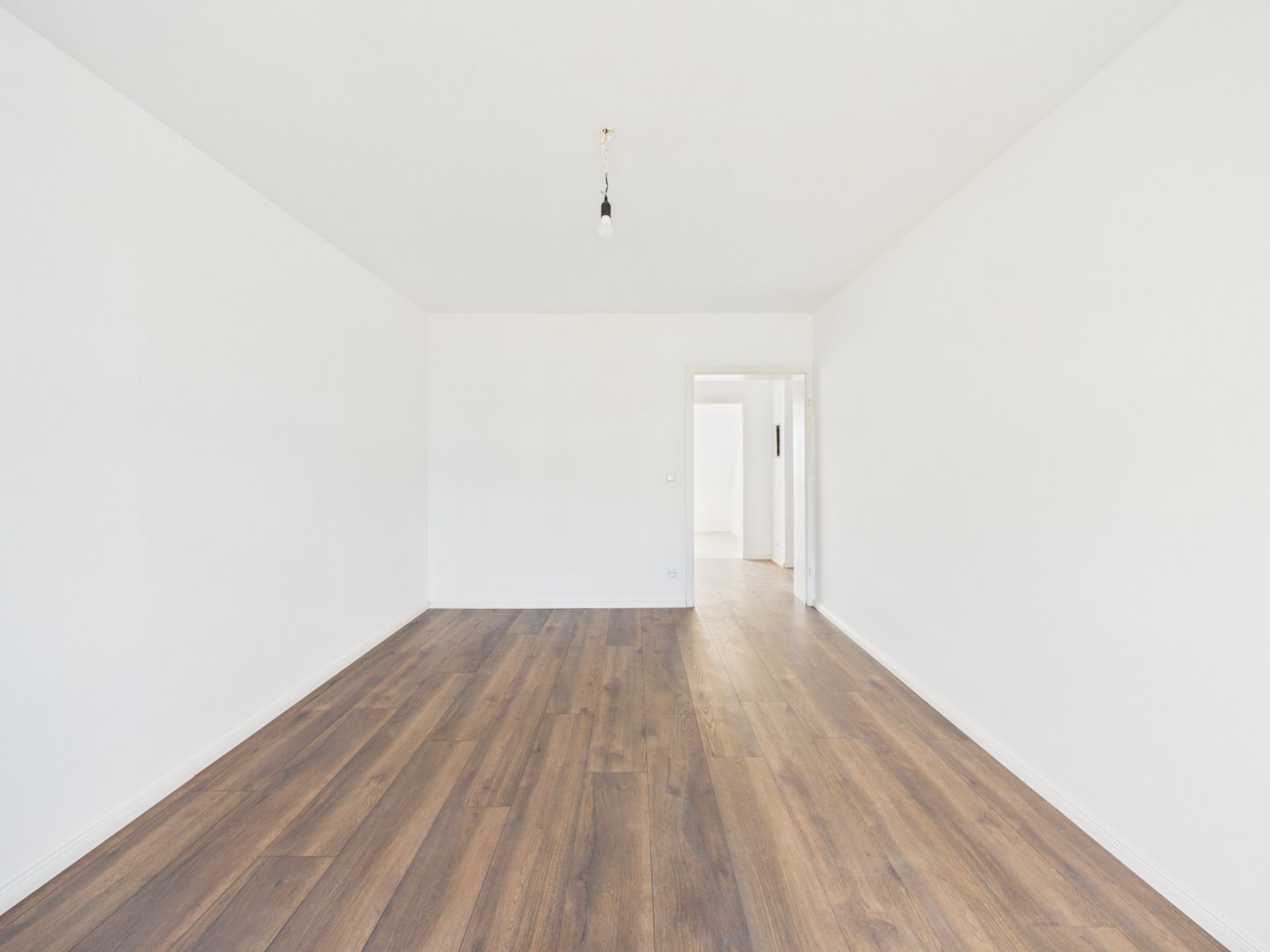 Leerer Raum mit weiß gestrichenen Wänden und dunklem Holzboden.