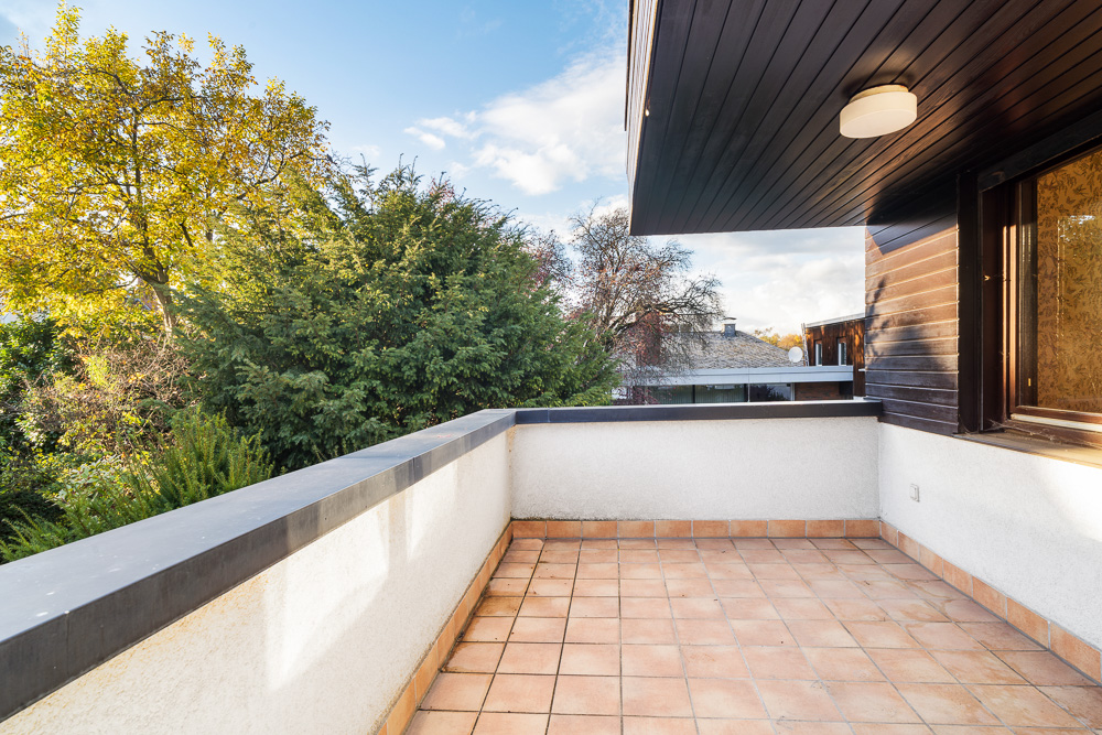 Große Terrasse mit Fliesenboden und weißem Geländer, umgeben von Bäumen.