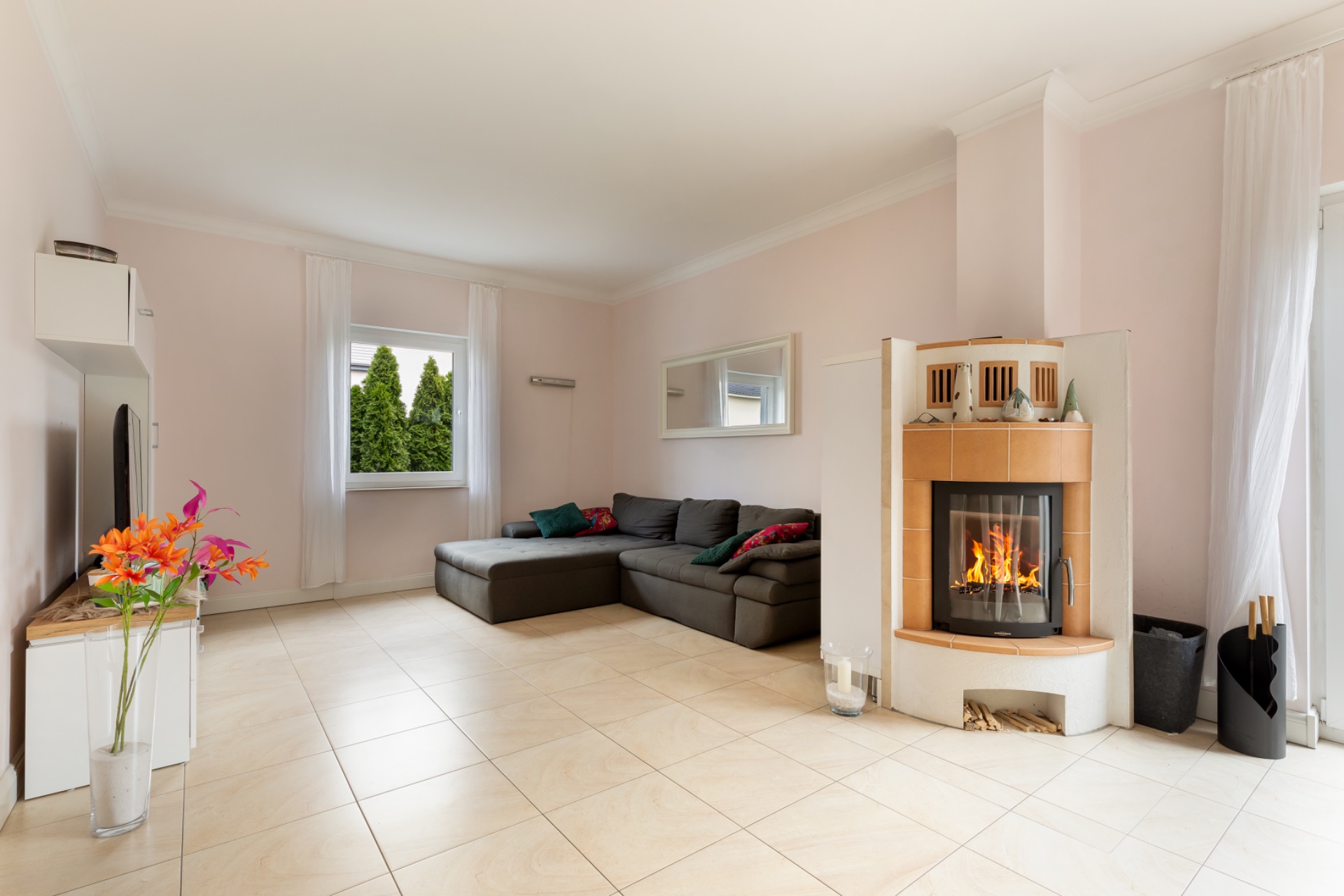 Helles Wohnzimmer mit Ecksofa, Kamin, Spiegel und großen Fenstern.